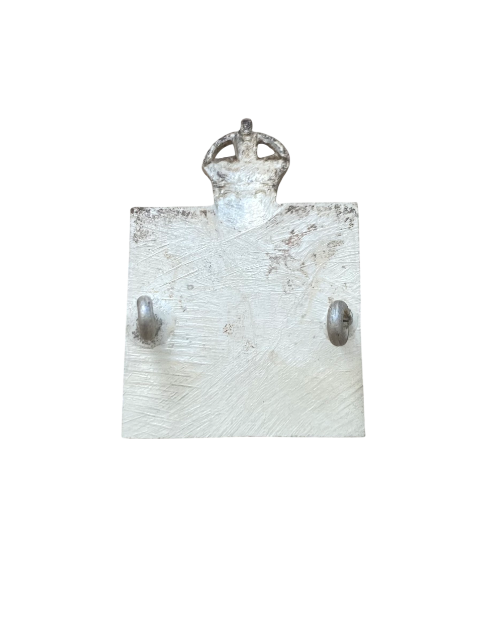 Reverse side of a silver badge with a cross design and crown on a white background